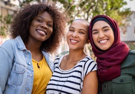 A group of three women of colour stand together smiling